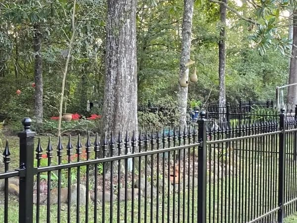 Black wrought iron fence with spear finials and post caps along a garden