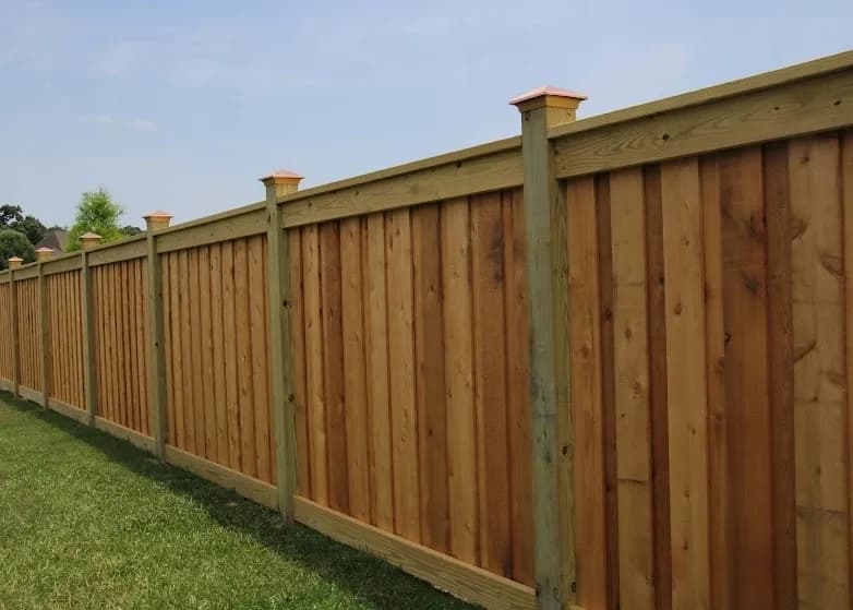 Wood board fence with copper post caps along a green lawn